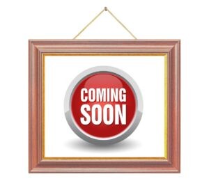 A wooden picture frame hangs on a wall in Northeast Albuquerque, displaying a red circular button with the words "COMING SOON" in bold white letters at the center.