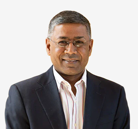 A man wearing glasses, a dark suit jacket, and a light-colored shirt stands smiling against a plain white background.