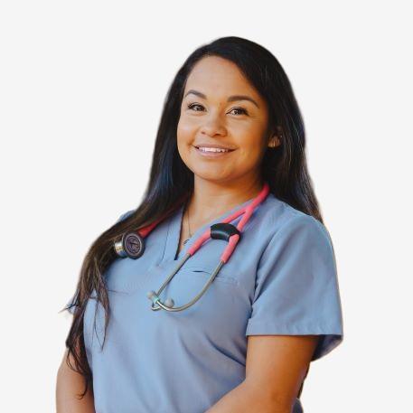 A woman in light blue scrubs with a pink stethoscope around her neck smiles at the camera against a plain white background.