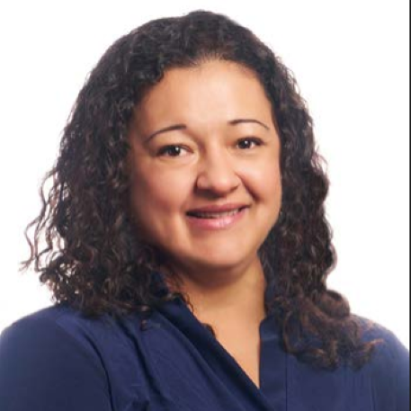 A woman with curly dark hair smiles at the camera in a dark blue top, posed against a plain white background. She brings the vibrant spirit of Westside Albuquerque to life with her warm and inviting expression.