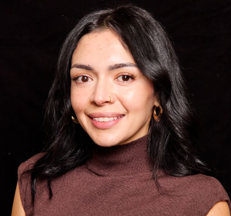 A woman with long dark hair, wearing a brown sleeveless turtleneck top and gold hoop earrings, smiles softly against a plain black background—professional like advance care practitioners & physician assistants in New Mexico.